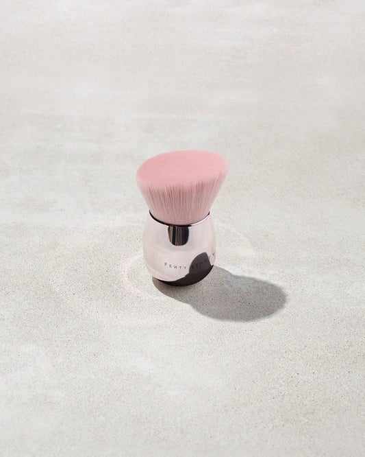 A fenty face and body kabuki brush with pink bristles on a gray background