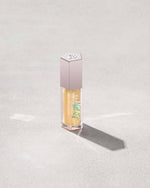 Closed tube of Gloss Bomb Heat lip gloss and plumper in the shade Lemon Lava on a grey background.