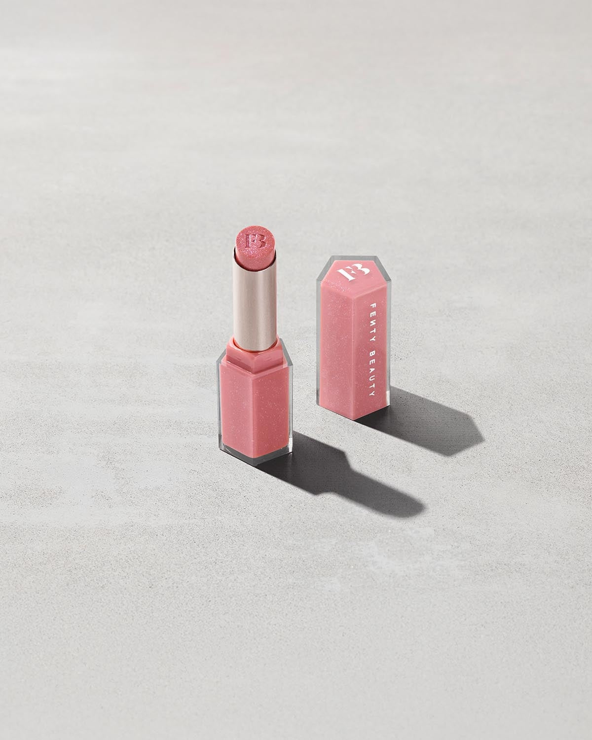 Open product shot of Gloss Bomb Stix Shimmer in shade Fussy on a concrete background.