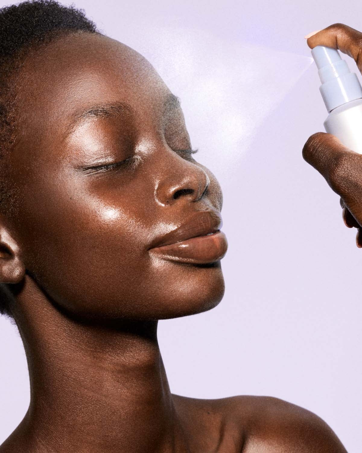 Person applying a lavender spray bottle to their face against a light purple background